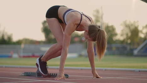 A-young-woman-athlete-brooding-warms-up-and-prepares-for-the-start-of-a-sprint-race-on-a-sunny-day-on-the-treadmill-of-the-stadium